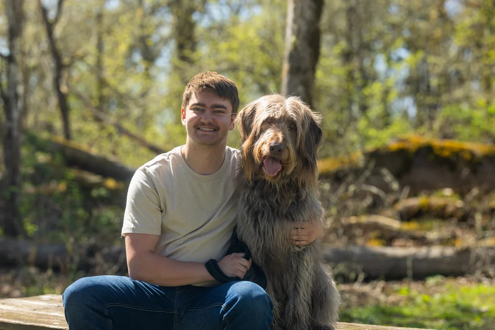 A smiling person and a dog in a sunlit forest