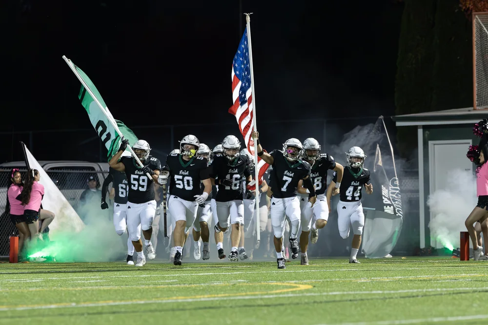 Football team entering the field through smoke with flags