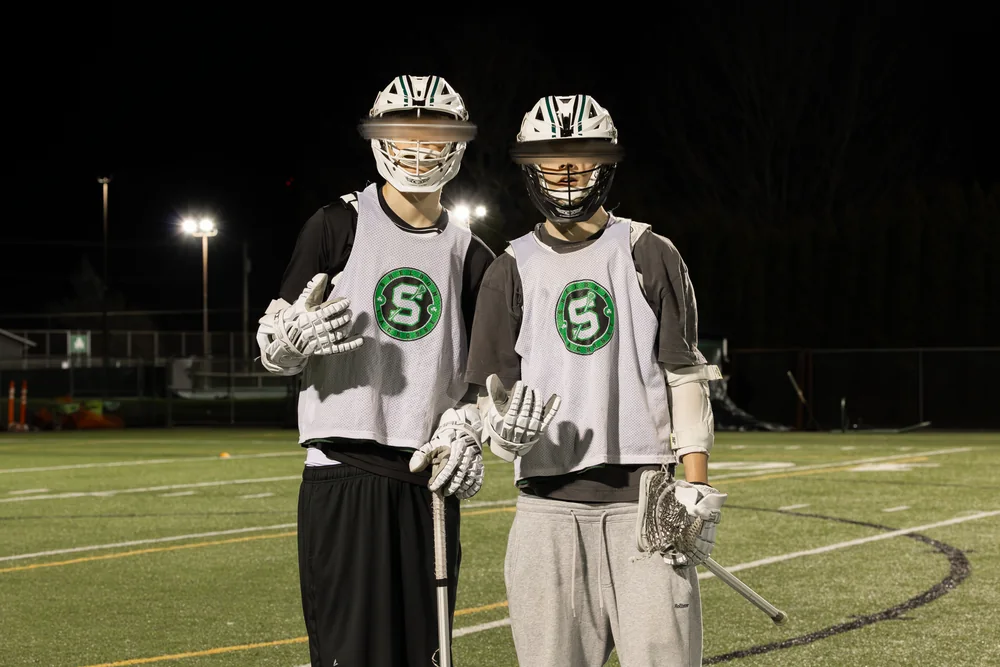 Two lacrosse players posing together on the field at night