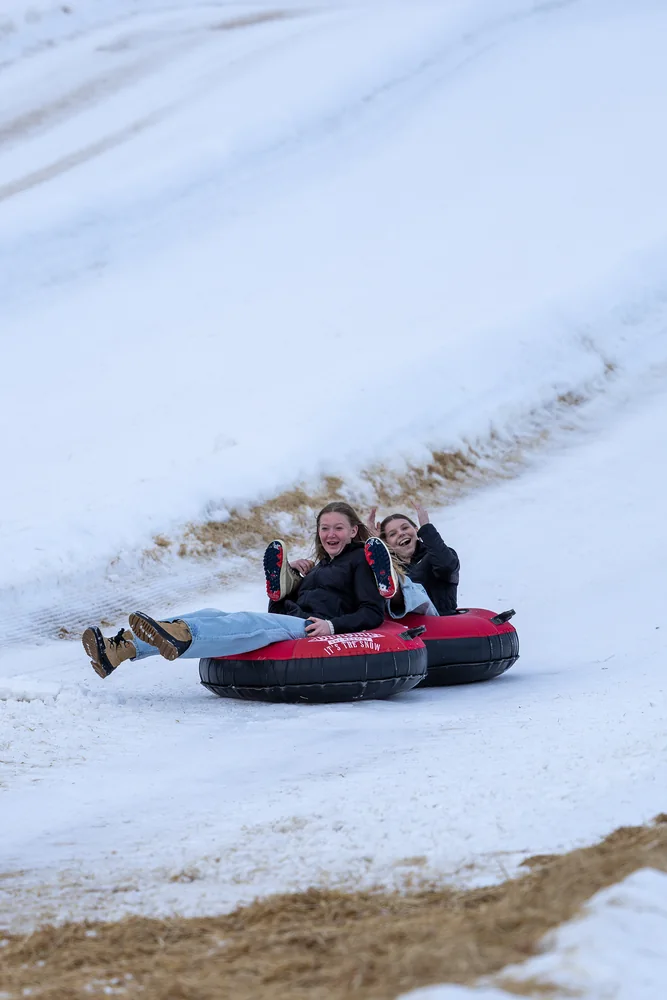 Two people riding a snow tube down a slope