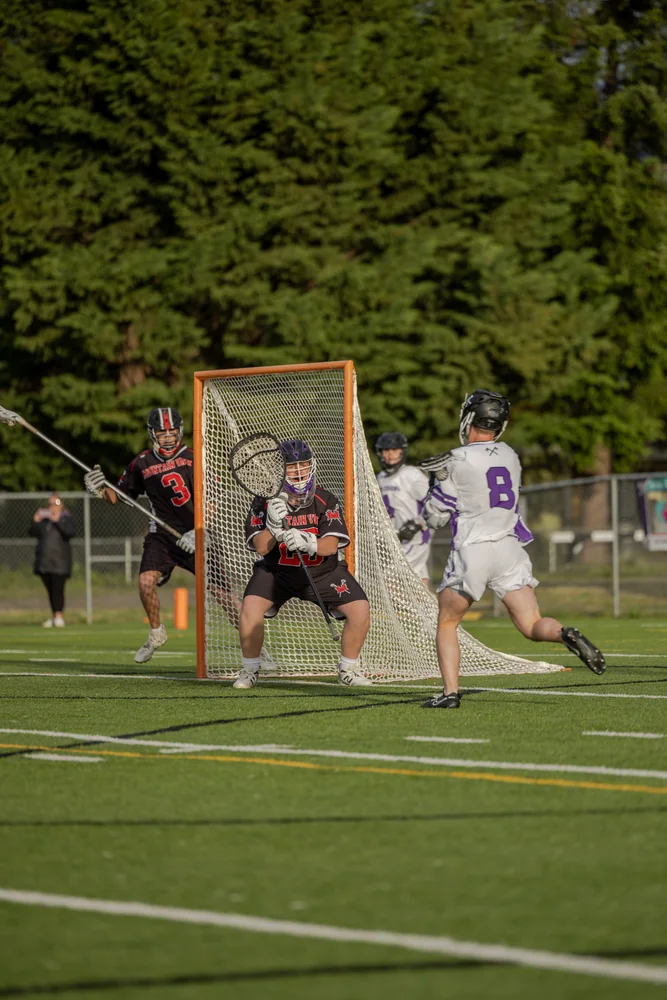 Lacrosse players competing on a field bordered by trees