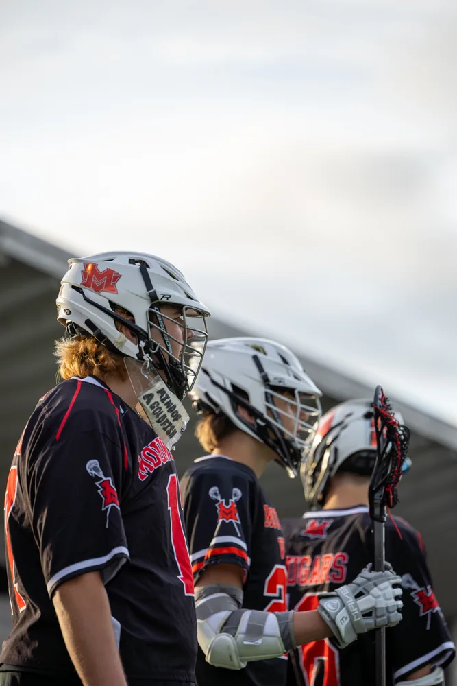 Helmeted lacrosse players on the sideline
