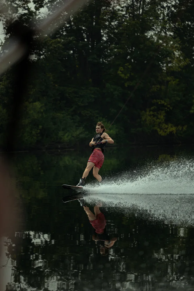 Wakeboarder cutting across the water beside a wooded shore